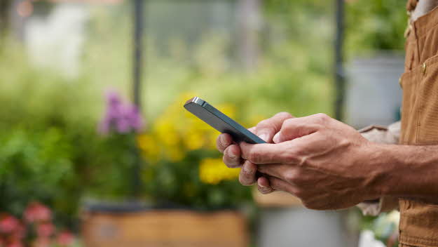 En person som håller i en telefon. I bakgrunden finns det blommor.