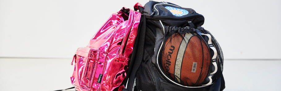 Två ryggsäckar på ett golv, en rosa och en svart med en synlig basketboll i