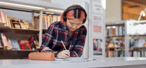 Ung tjej som sitter och skriver på ett block med hörlurar i en studiemiljö