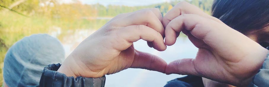 Barnhänder formade som ett hjärta med regnbågen i bakgrunden.