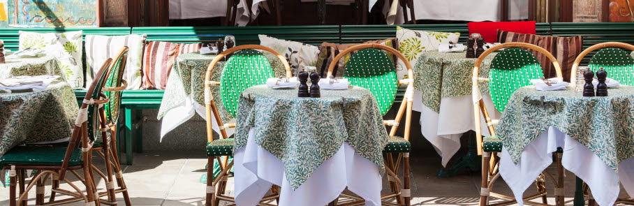 Uteservering, små runda bord med grön duk. Och två stolar vid bordet. 