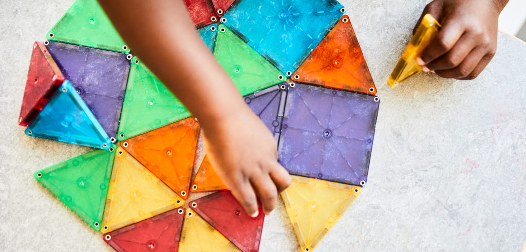 Barnhänder lägger en form av färgglada plastbrickori