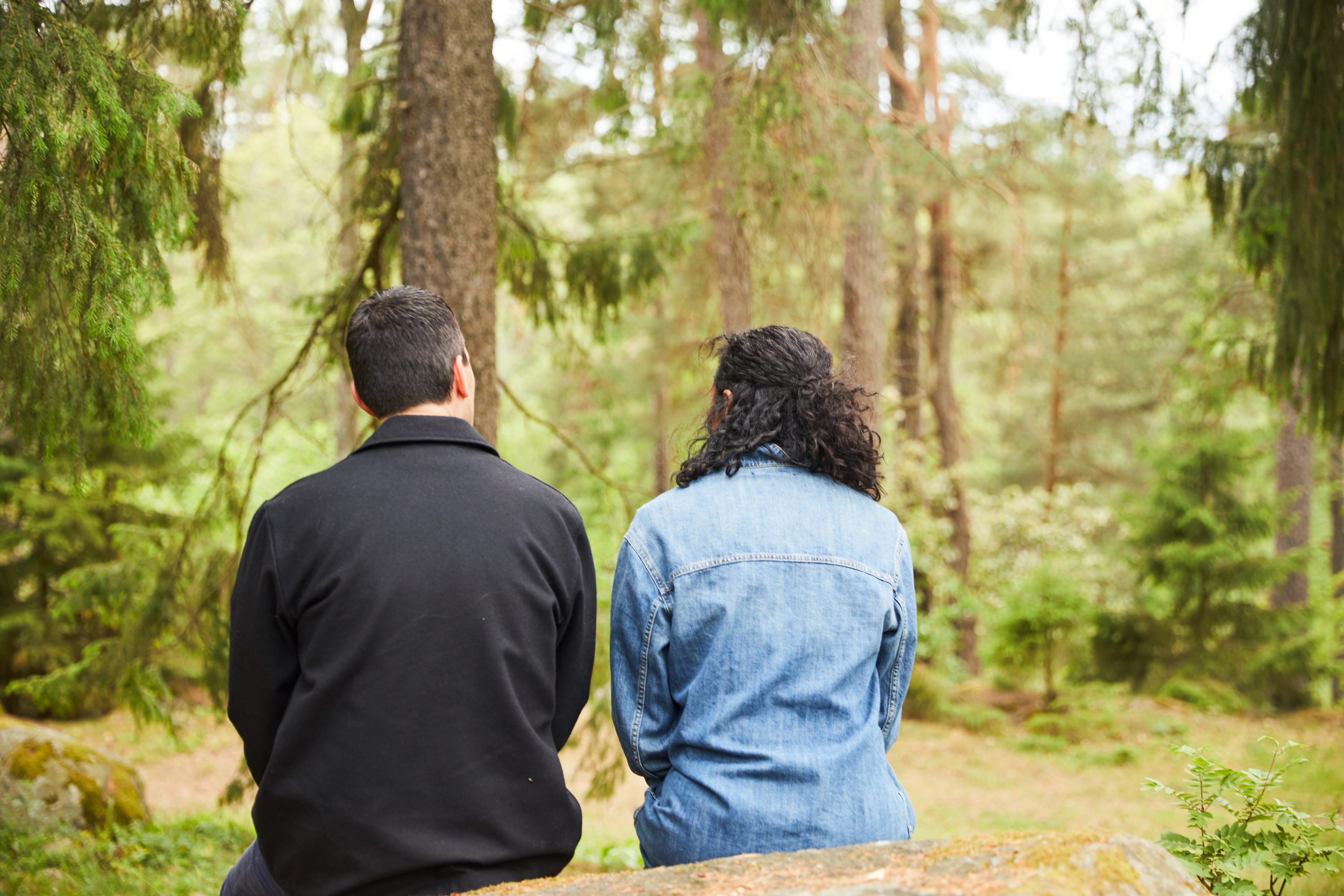 Kvinna och man bakifrån, sitter på stor sten i skog