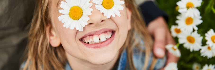 Glad flicka med blommor lagda över ögonen